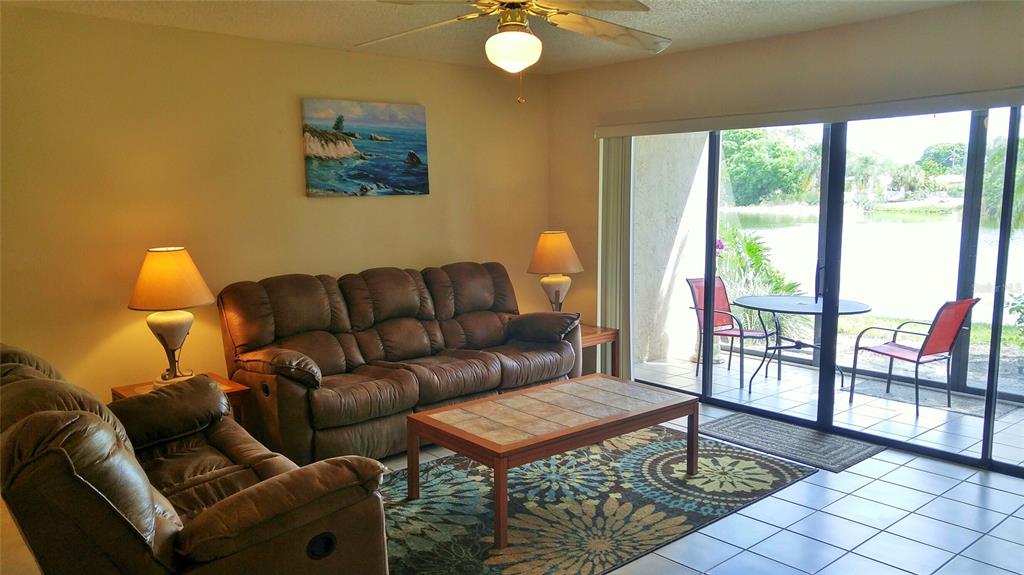 A living room features brown leather furniture, a patterned rug, and sliding doors to a patio — 5677 ASHTON LAKE DRIVE UNIT 11, SARASOTA, FL