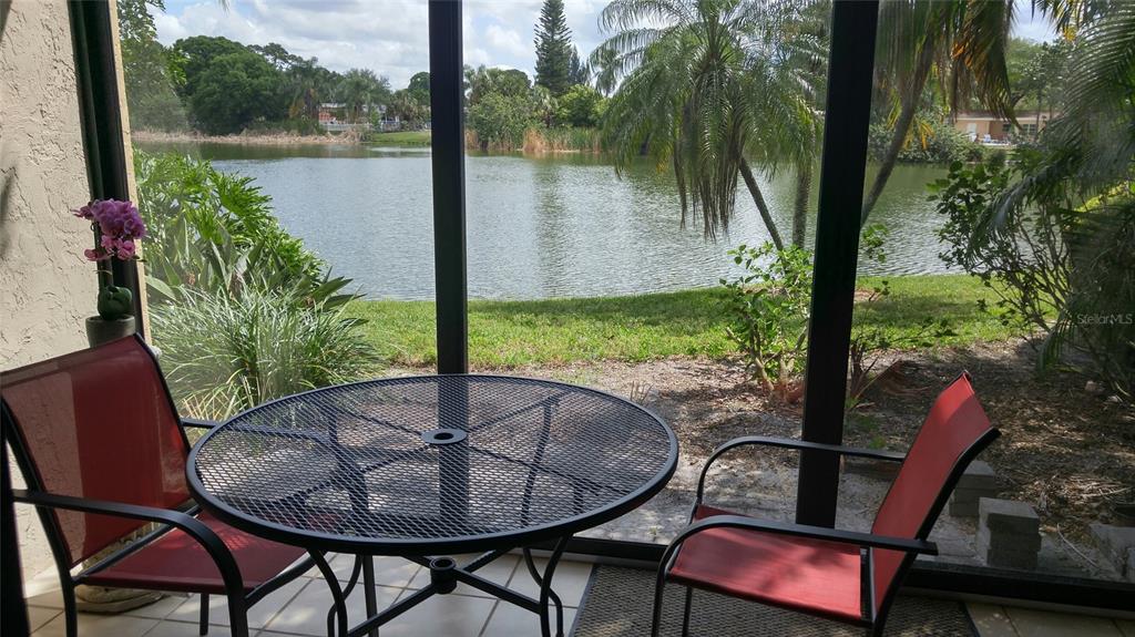 A screened-in patio features a metal table and chairs overlooking a lake and palm trees — 5677 ASHTON LAKE DRIVE UNIT 11, SARASOTA, FL
