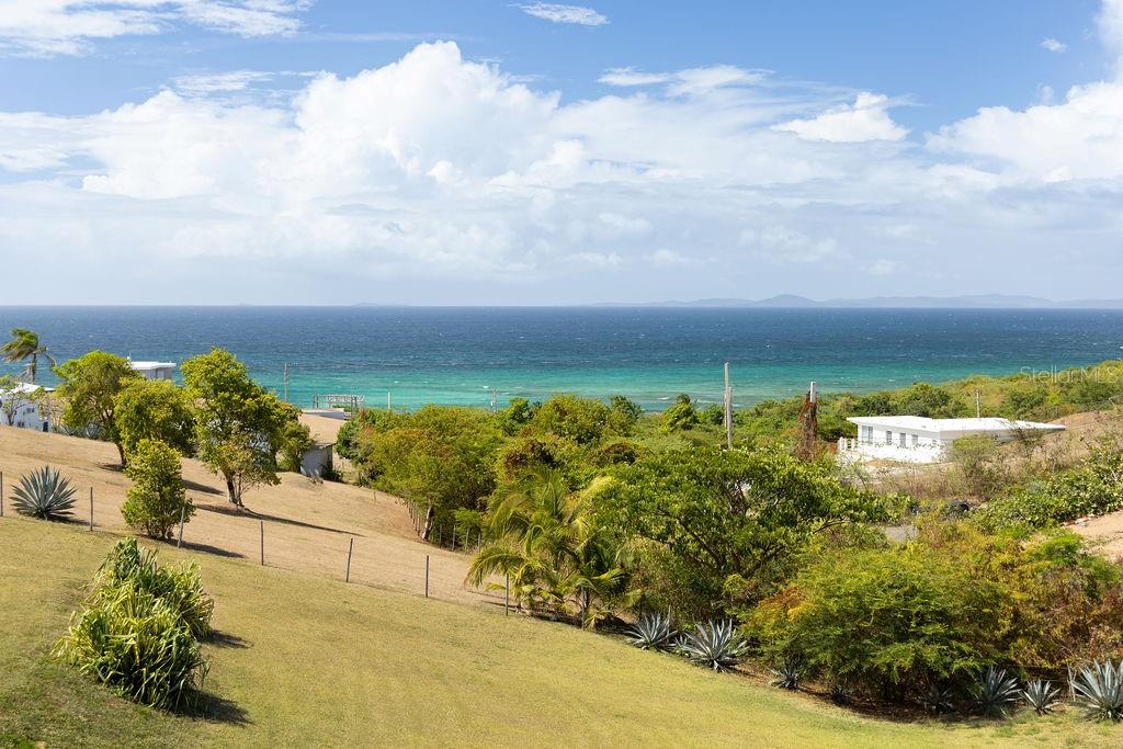 A grassy hillside slopes down toward a coastal view of the ocean and distant islands — 759B COM. VILLA BORINQUEN, VIEQUES, PR
