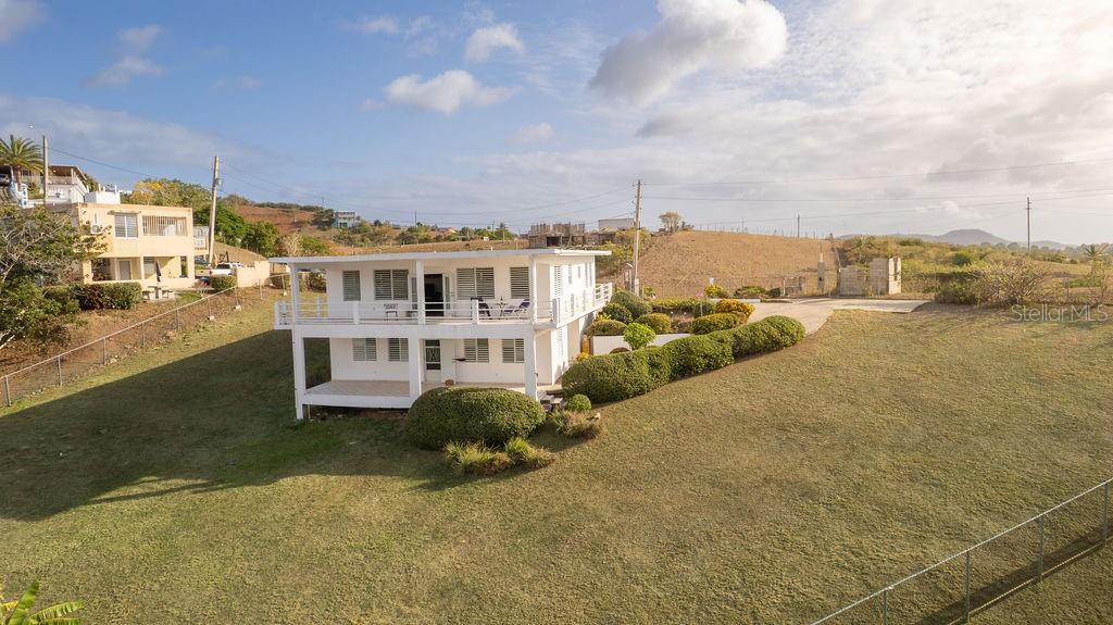 A two-story white house with a balcony sits on a large, grassy hillside lot — 759B COM. VILLA BORINQUEN, VIEQUES, PR