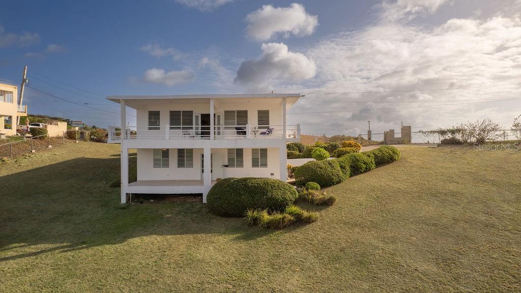 A two-story white house with a balcony sits on a grassy hillside — 759B COM. VILLA BORINQUEN, VIEQUES, PR