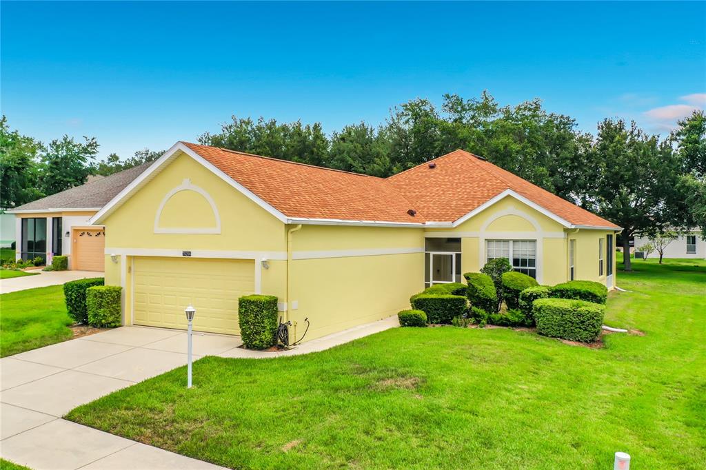 A yellow single-story house with a two-car garage and a brown shingled roof — 25206 ORMOND COURT, LEESBURG, FL