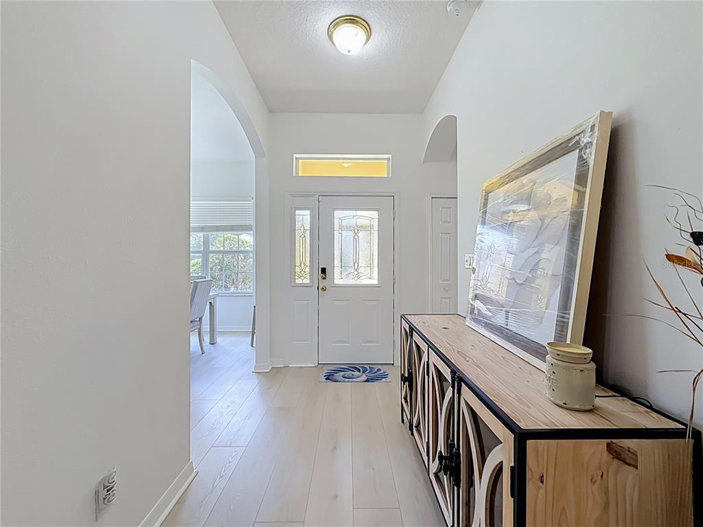 A bright entryway features light wood-look flooring, a white front door, and a wooden console — 25206 ORMOND COURT, LEESBURG, FL