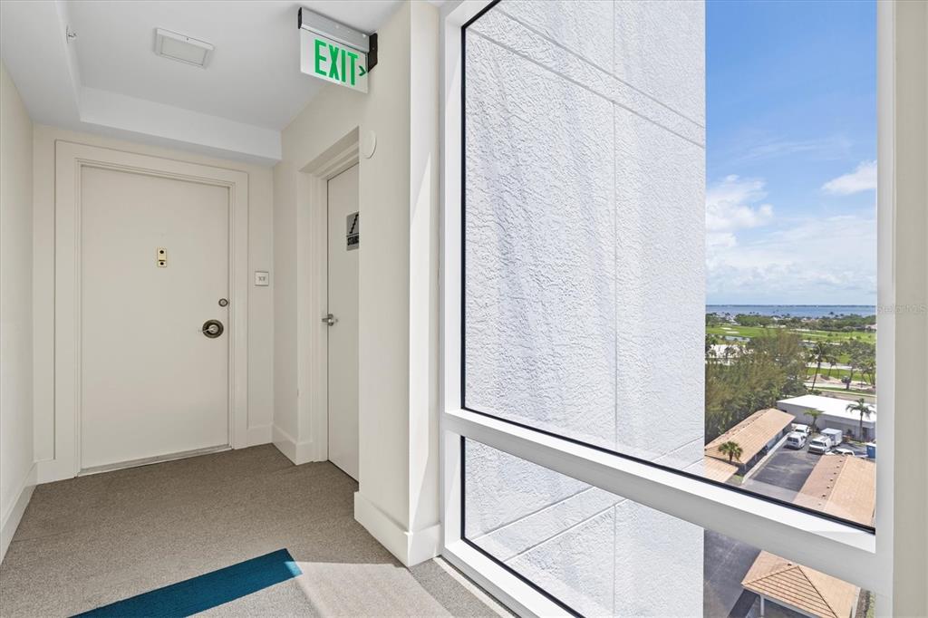 A hallway with a white door, an exit sign, and a large window overlooking the coast — 2425 GULF OF MEXICO DRIVE UNIT 10F, LONGBOAT KEY, FL