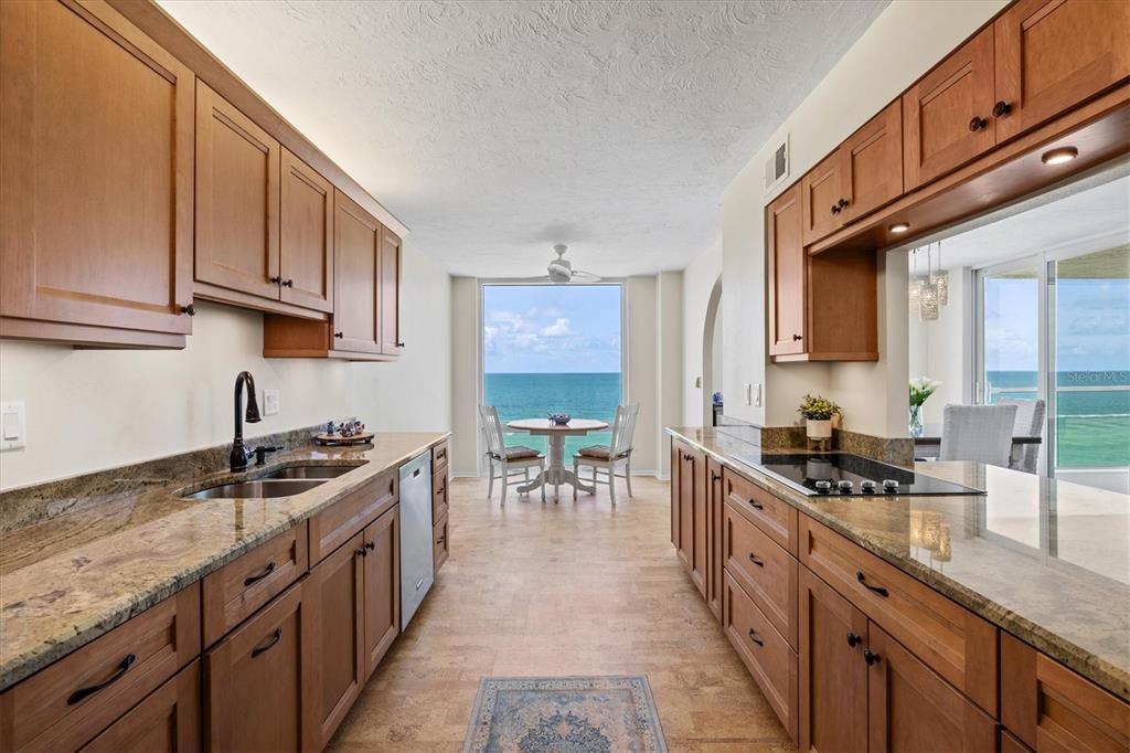 A galley kitchen with wood cabinets and granite countertops leads to a dining area with ocean views — 2425 GULF OF MEXICO DRIVE UNIT 10F, LONGBOAT KEY, FL