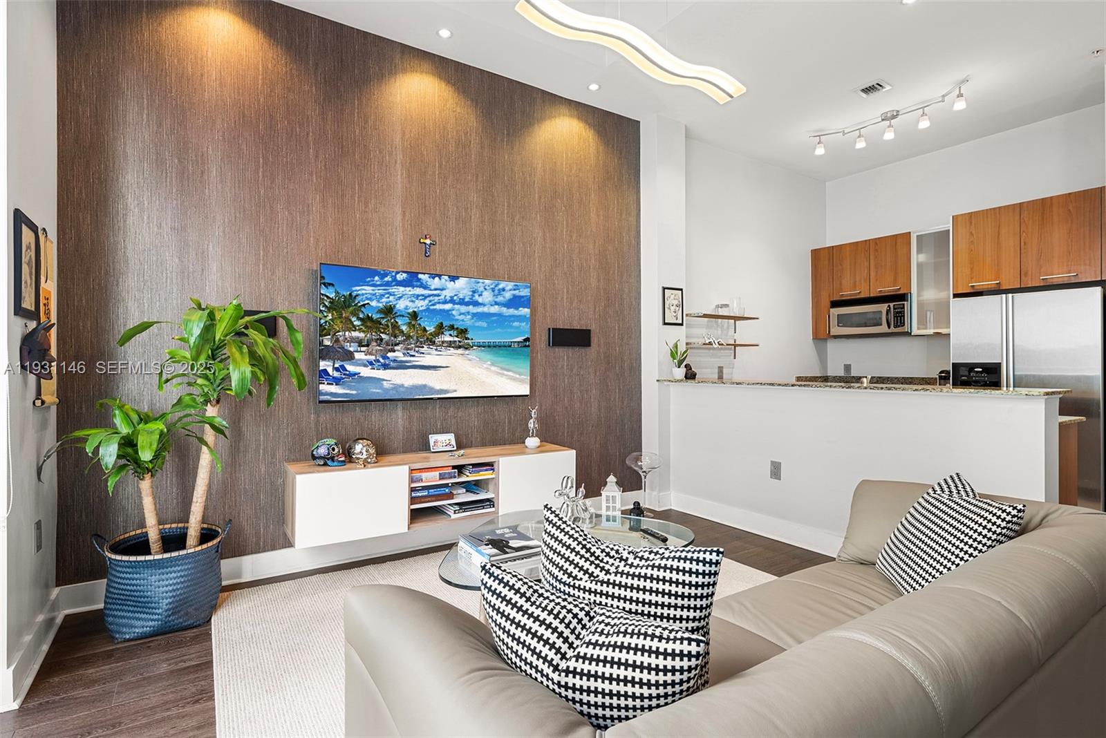 A living room features a wood-paneled accent wall, a wall-mounted television, and an open kitchen — 9066 SW 73rd Ct # 405, Miami FL 33156, MIAMI, FL