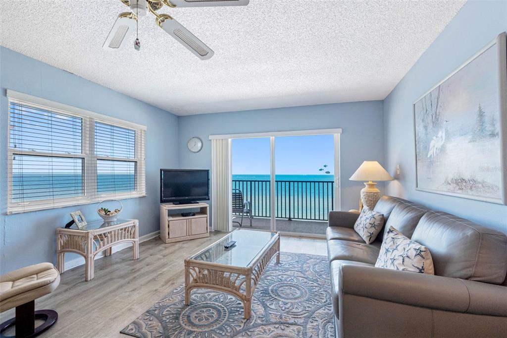A living room with light blue walls, a grey sofa, and a view of the ocean — 14300 GULF BOULEVARD UNIT 501, MADEIRA BEACH, FL