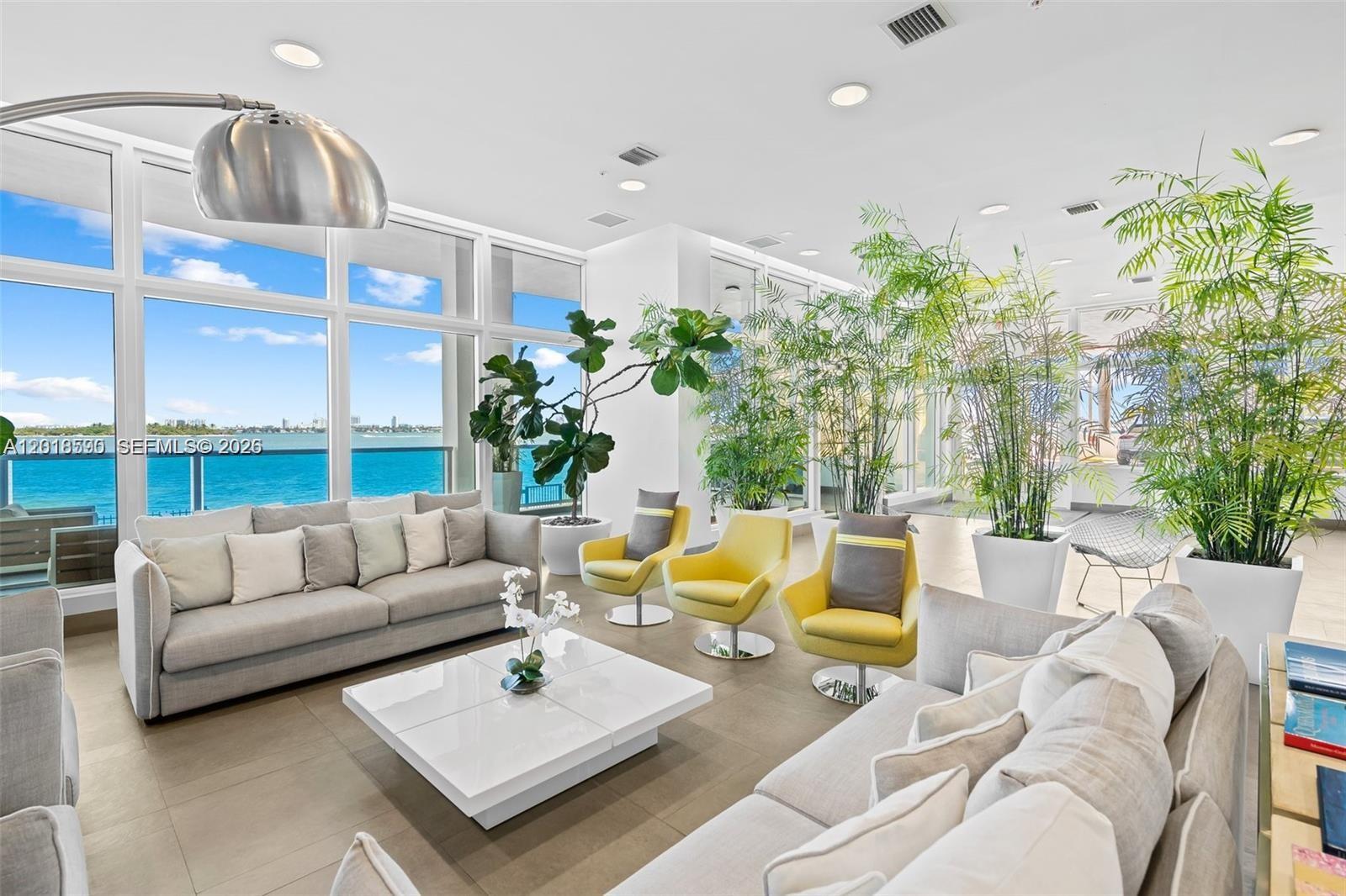 A bright living room features floor-to-ceiling windows overlooking the ocean, sofas, and potted plants — 725 NE 22nd St, Miami FL 33137, MIAMI, FL