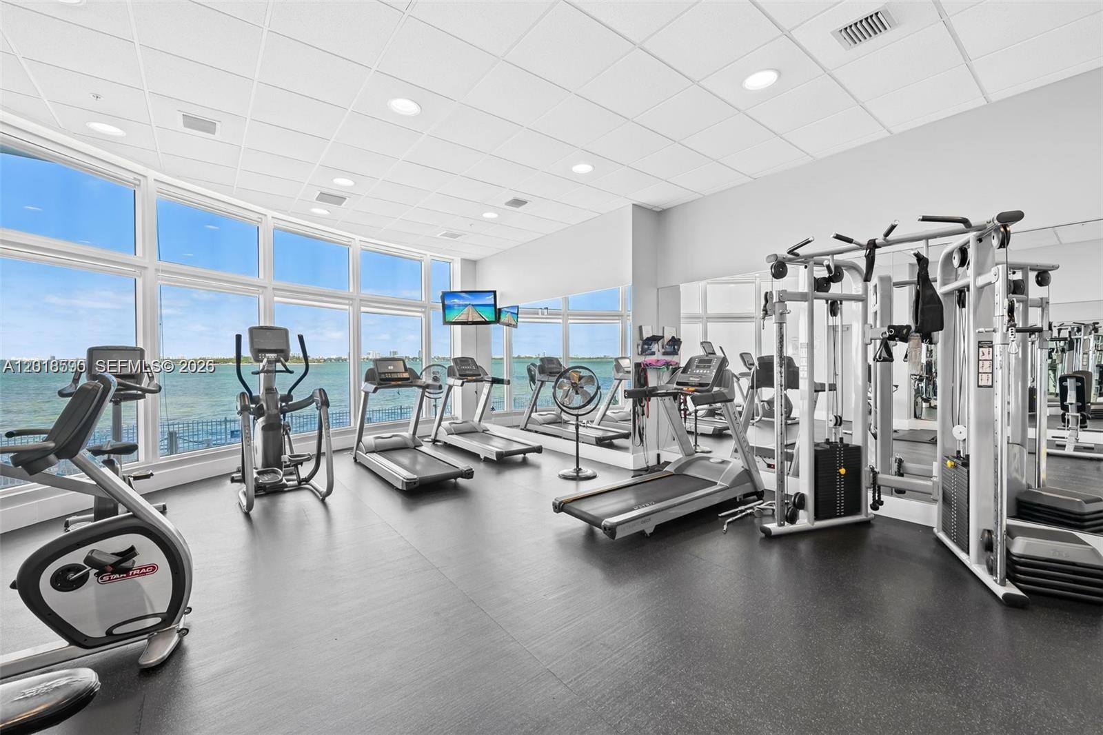 A gym features various exercise machines, large windows overlooking the water, and mirrored walls — 725 NE 22nd St, Miami FL 33137, MIAMI, FL