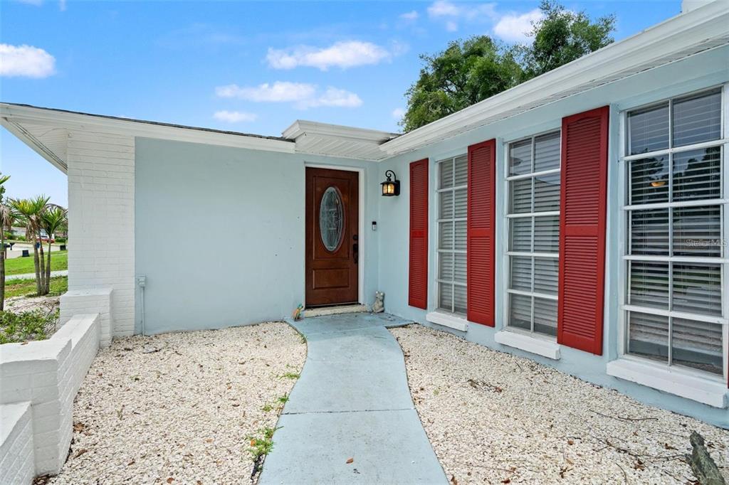A light blue house exterior features a brown front door, red shutters, and gravel landscaping — 7710 BIRCHWOOD DRIVE, PORT RICHEY, FL