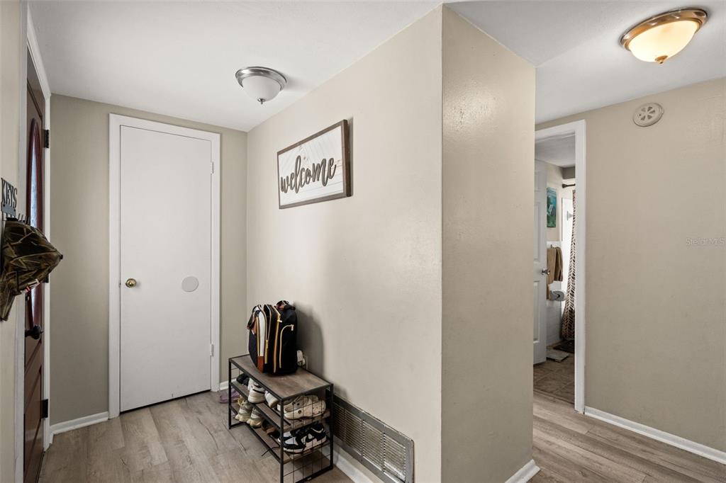 An entryway features light wood-look flooring, a white door, a shoe rack, and a welcome sign — 7710 BIRCHWOOD DRIVE, PORT RICHEY, FL
