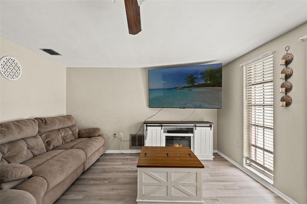 A living room features a brown sofa, a white media console with a fireplace, and wood-look flooring — 7710 BIRCHWOOD DRIVE, PORT RICHEY, FL
