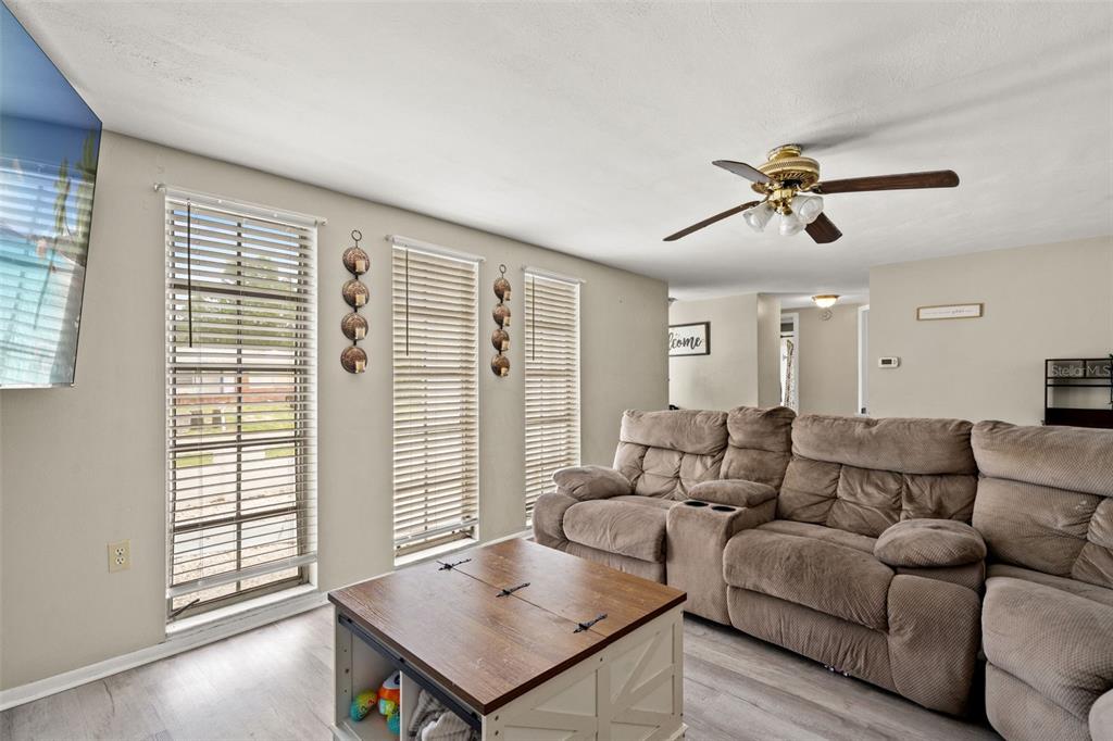 A living room features a brown sectional sofa, a wooden coffee table, and three windows — 7710 BIRCHWOOD DRIVE, PORT RICHEY, FL