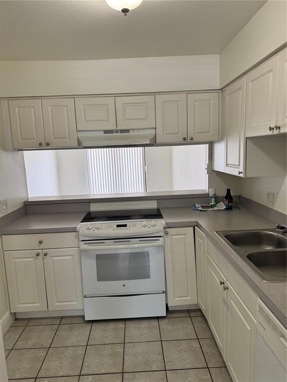 A kitchen features white cabinetry, a white electric range, and gray countertops over tiled floors — 2219 CARIBBEAN DRIVE S UNIT 27, KISSIMMEE, FL