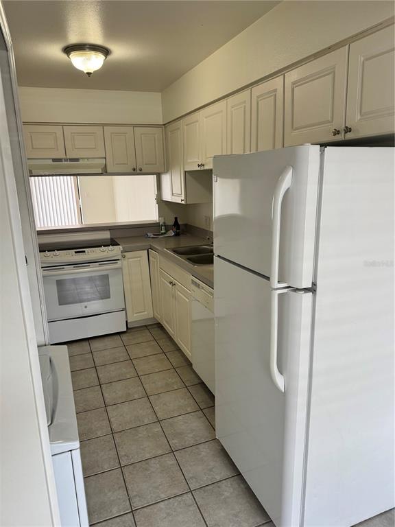 A kitchen features white cabinets, white appliances, tile flooring, and a pass-through window — 2219 CARIBBEAN DRIVE S UNIT 27, KISSIMMEE, FL