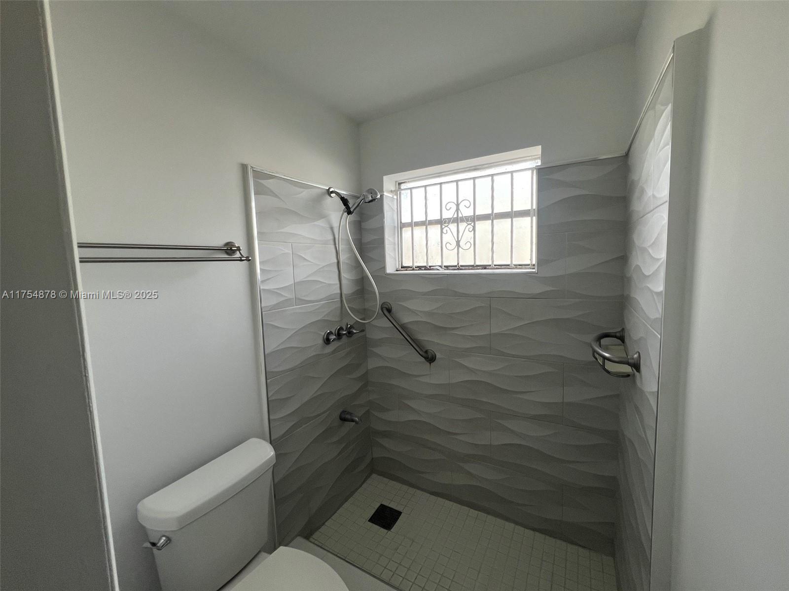 A bathroom features a walk-in shower with textured gray tiles, a grab bar, and a window — 887 W 29th St # 2, Hialeah FL 33012, HIALEAH, FL