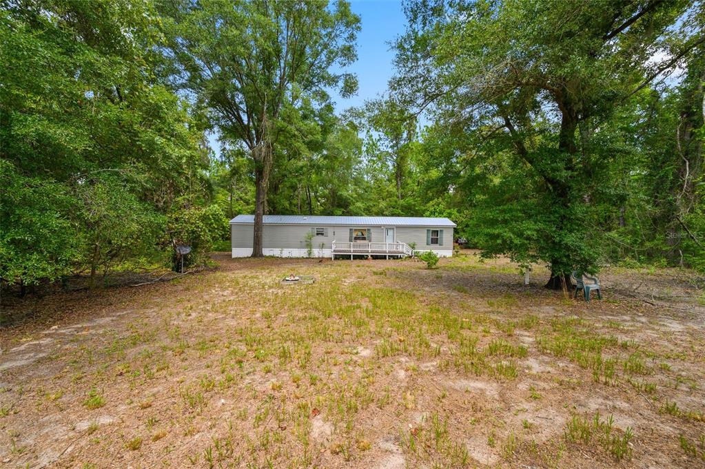 A single-story manufactured home sits in a clearing surrounded by dense trees and foliage — 25697 21ST ROAD, O'BRIEN, FL