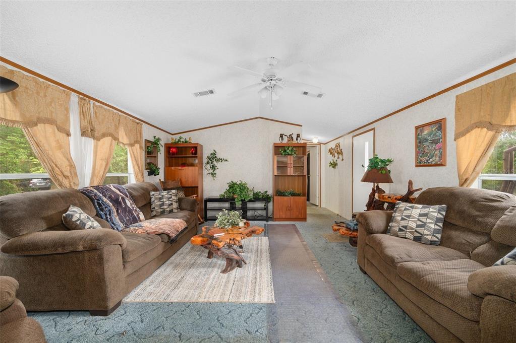 A living room features two brown sofas, a wood coffee table, and beige patterned wallpaper — 25697 21ST ROAD, O'BRIEN, FL