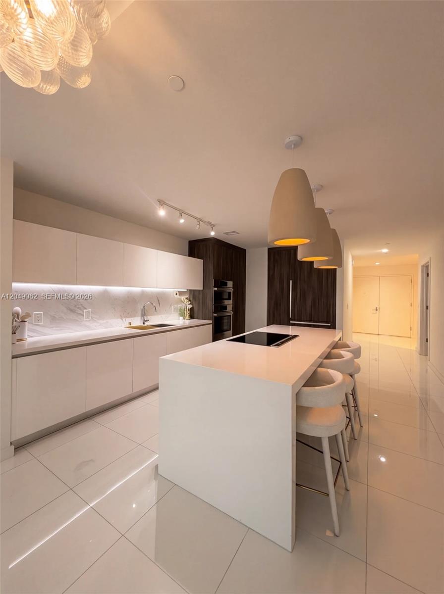 A modern kitchen features white cabinetry, a central island with bar seating, and tile flooring — 851 NE 1st Ave # 2301, Miami FL 33132, MIAMI, FL