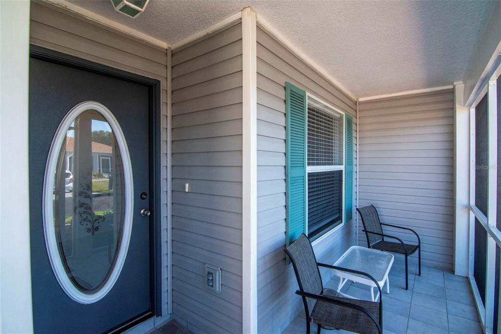 A covered porch features gray vinyl siding, a dark door with an oval window, and furniture — 29236 KAPALUA WAY, SAN ANTONIO, FL
