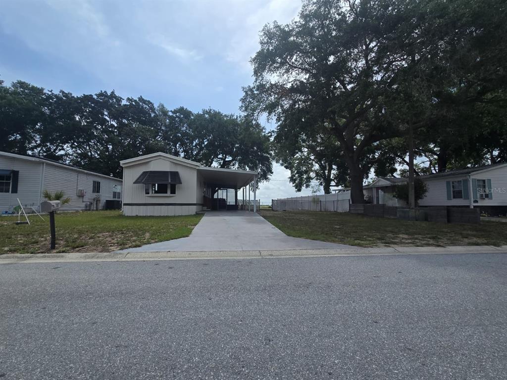 A single-story mobile home with a concrete driveway and a carport under large trees — 1807 PAULINE DRIVE UNIT 279, LAKE ALFRED, FL