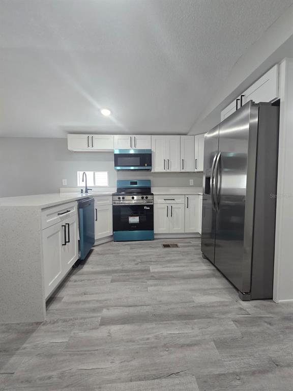 A kitchen with white cabinets, stainless steel appliances, quartz countertops, and gray wood-look flooring — 1807 PAULINE DRIVE UNIT 279, LAKE ALFRED, FL