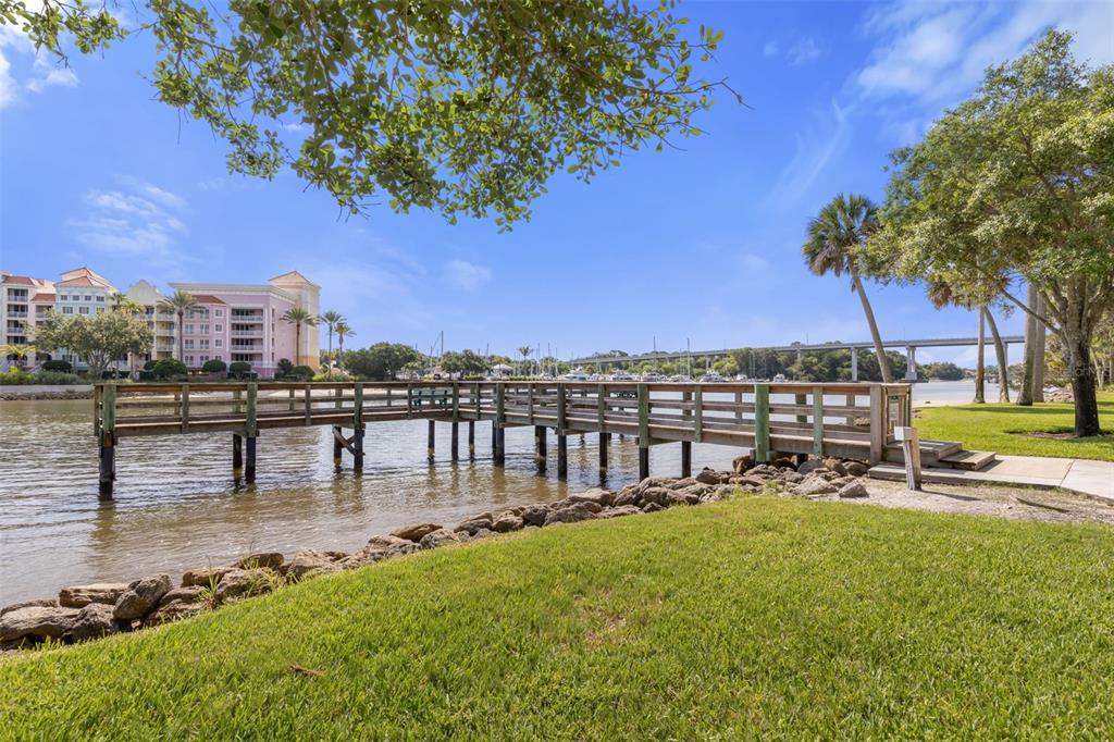 A wooden pier extends into a river with a bridge and buildings in the background — 146 PALM COAST RESORT BOULEVARD UNIT 107, PALM COAST, FL