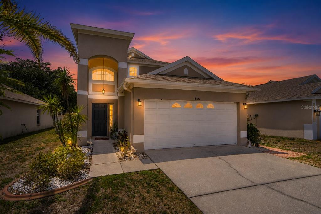 A two-story suburban house with a tan stucco exterior, a two-car garage, and a sunset — 8526 HAWBUCK STREET, TRINITY, FL