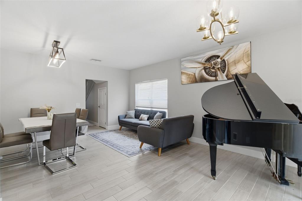 A living and dining area features a grand piano, gray sofa, and modern light fixtures — 8526 HAWBUCK STREET, TRINITY, FL
