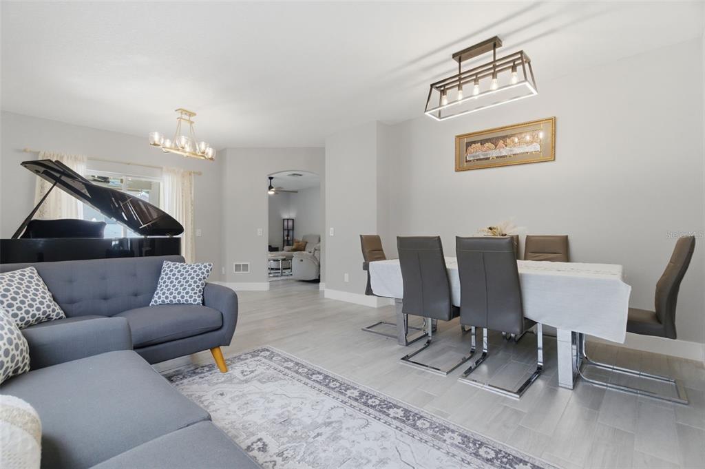 A dining area and living space feature a grand piano, gray sofa, and modern lighting — 8526 HAWBUCK STREET, TRINITY, FL