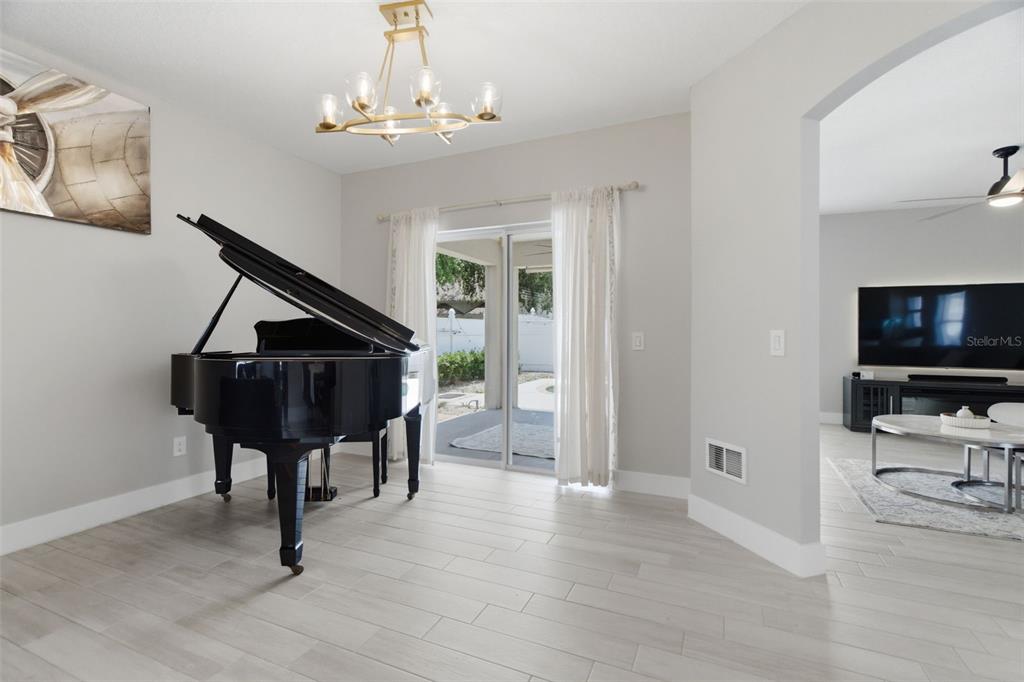 A dining room with a grand piano, light wood-look tile floors, and a sliding glass door — 8526 HAWBUCK STREET, TRINITY, FL