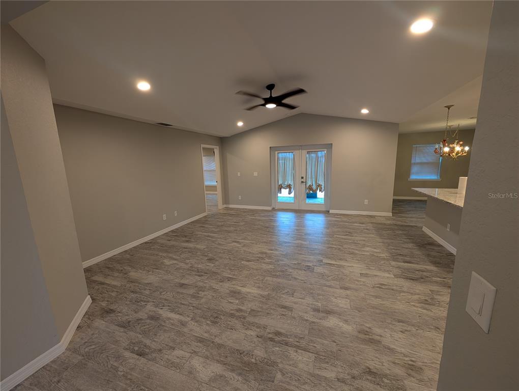 A spacious living room features vaulted ceilings, gray wood-look flooring, and glass double doors — 12190 KNEELAND TERRACE, PORT CHARLOTTE, FL