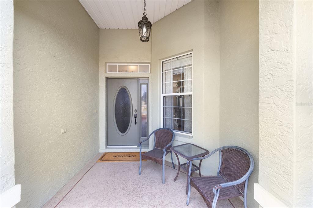 A covered front porch features a gray front door, a window, and two wicker chairs — 8785 SW 82ND COURT ROAD, OCALA, FL