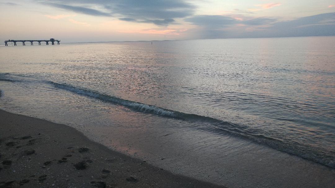 A sandy beach meets the calm ocean at sunset with a pier in the distance — 7507 S Indian River Dr, Fort Pierce FL 34982, FORT PIERCE, FL