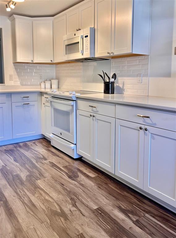 A kitchen features white cabinets, a white stove, a microwave, and wood-look flooring — 984 SUNRIDGE DRIVE UNIT J3, SARASOTA, FL