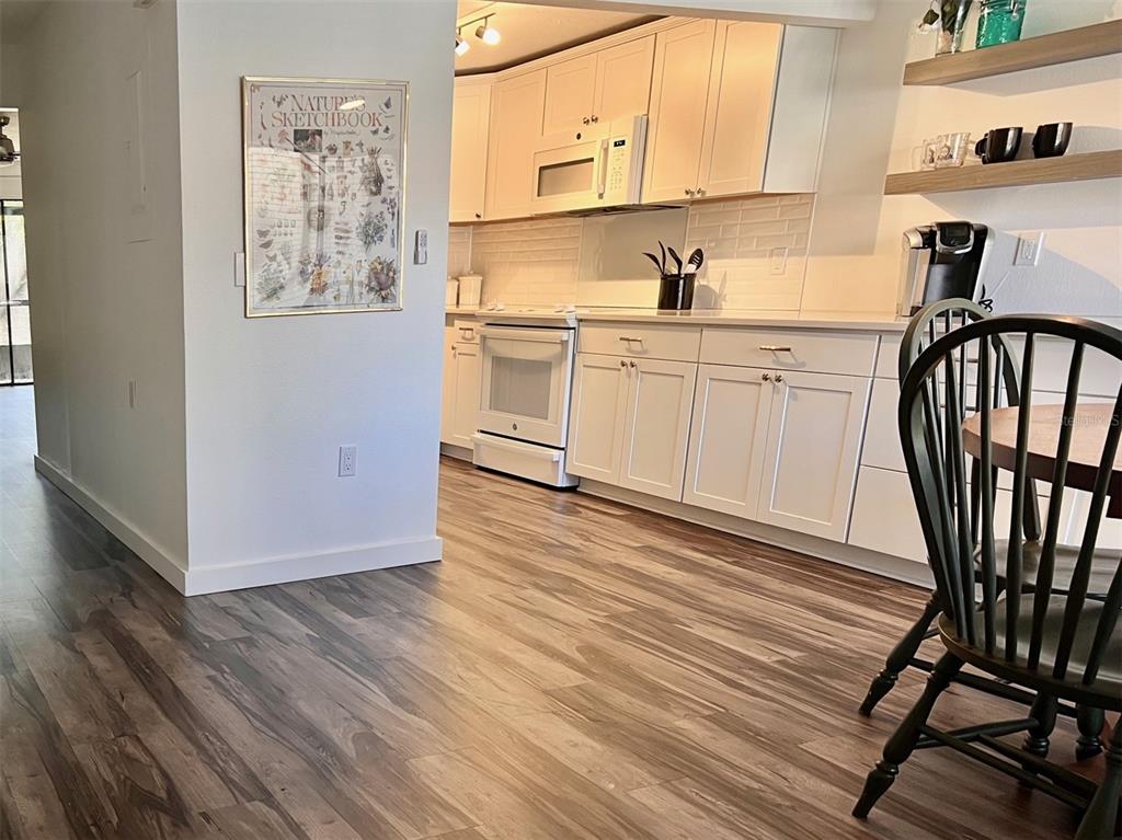 A kitchen with white cabinets, white appliances, and wood-look flooring, viewed from an adjacent room — 984 SUNRIDGE DRIVE UNIT J3, SARASOTA, FL