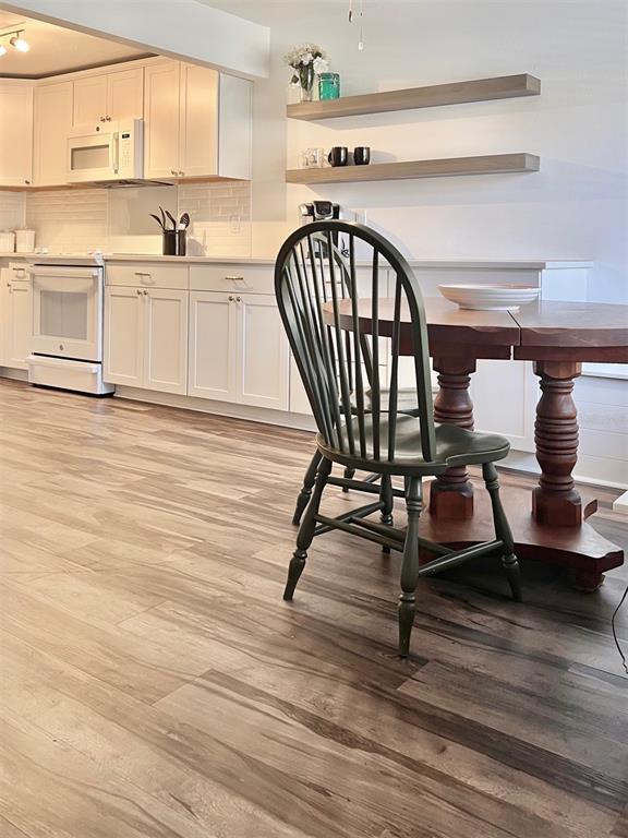 A kitchen features white cabinetry, wood-look flooring, and a round wooden dining table with chairs — 984 SUNRIDGE DRIVE UNIT J3, SARASOTA, FL
