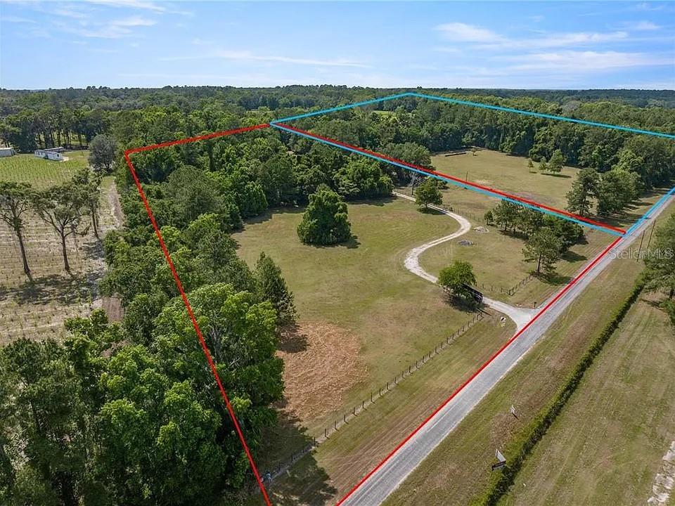 An aerial view shows a large, grassy lot with trees and a dirt driveway — TBD NW 65TH AVENUE ROAD, REDDICK, FL