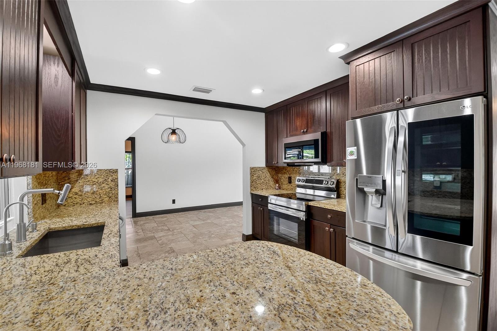 A kitchen features dark wood cabinets, granite countertops, stainless steel appliances, and tile flooring — 13808 Geranium Pl, Wellington FL 33414, WELLINGTON, FL