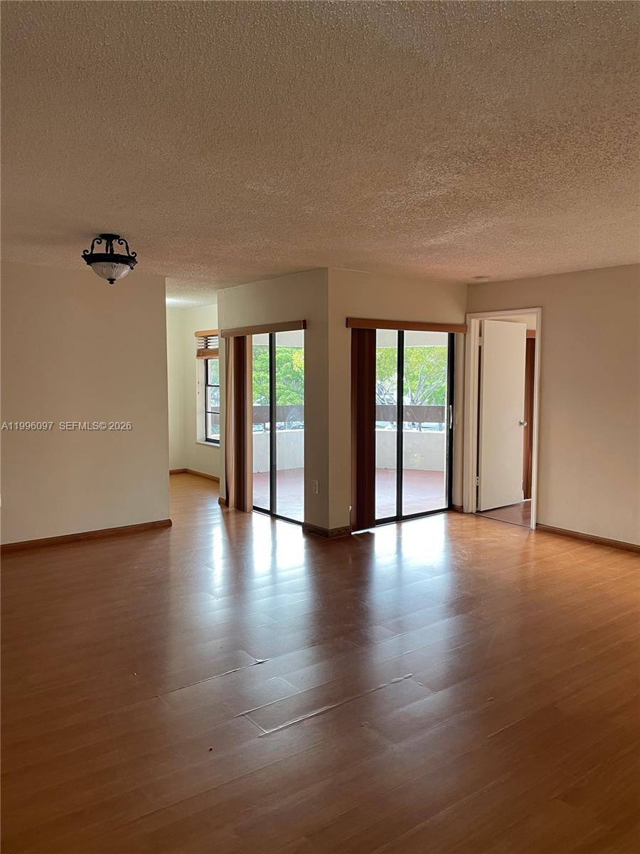 A living room with wood-look flooring features two sliding glass doors leading to a balcony — 9140 SW 123rd Ct # 309, Miami FL 33186, MIAMI, FL
