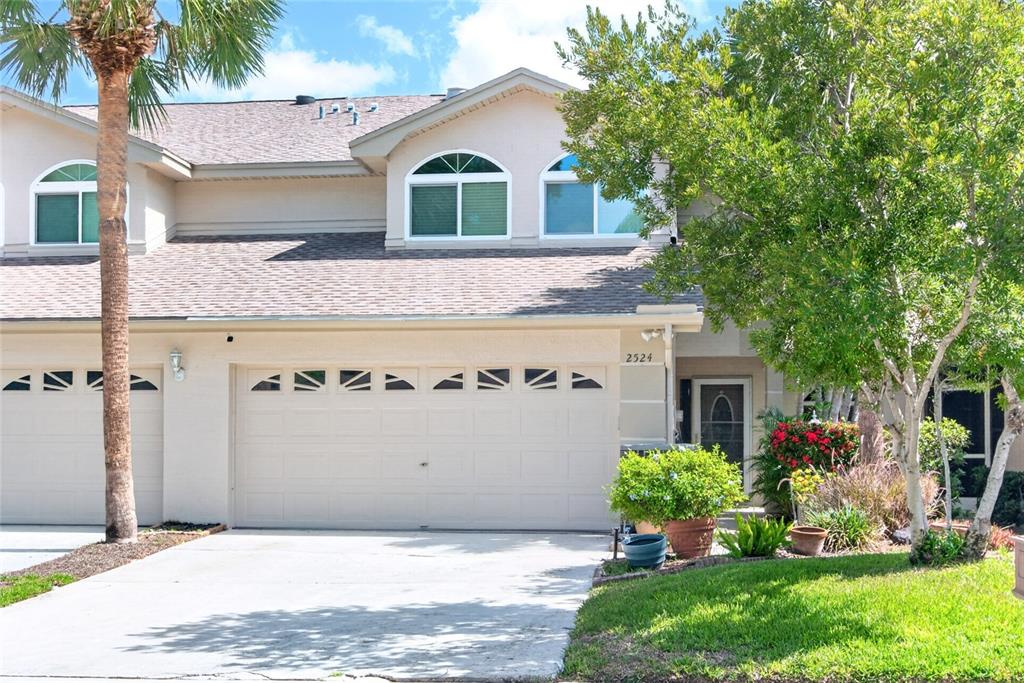 A two-story townhouse exterior features a beige facade, a two-car garage, and arched windows — 2524 W BROOK LANE, CLEARWATER, FL