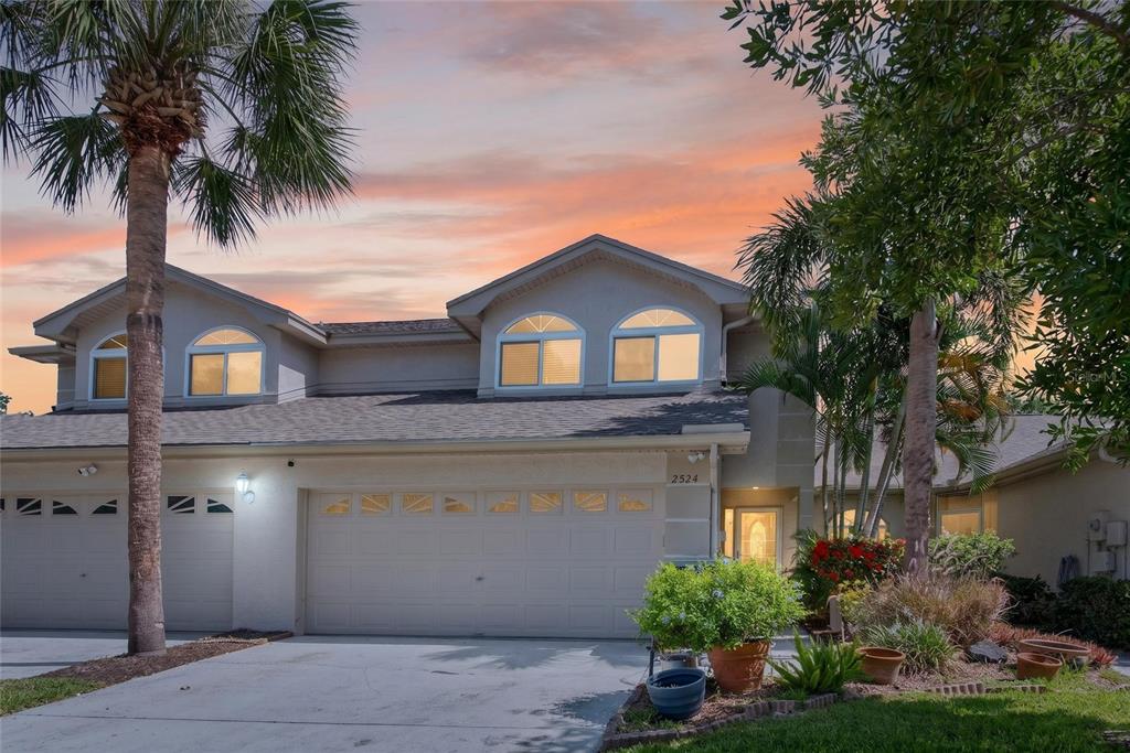 A two-story townhouse with a two-car garage and arched windows under a sunset sky — 2524 W BROOK LANE, CLEARWATER, FL