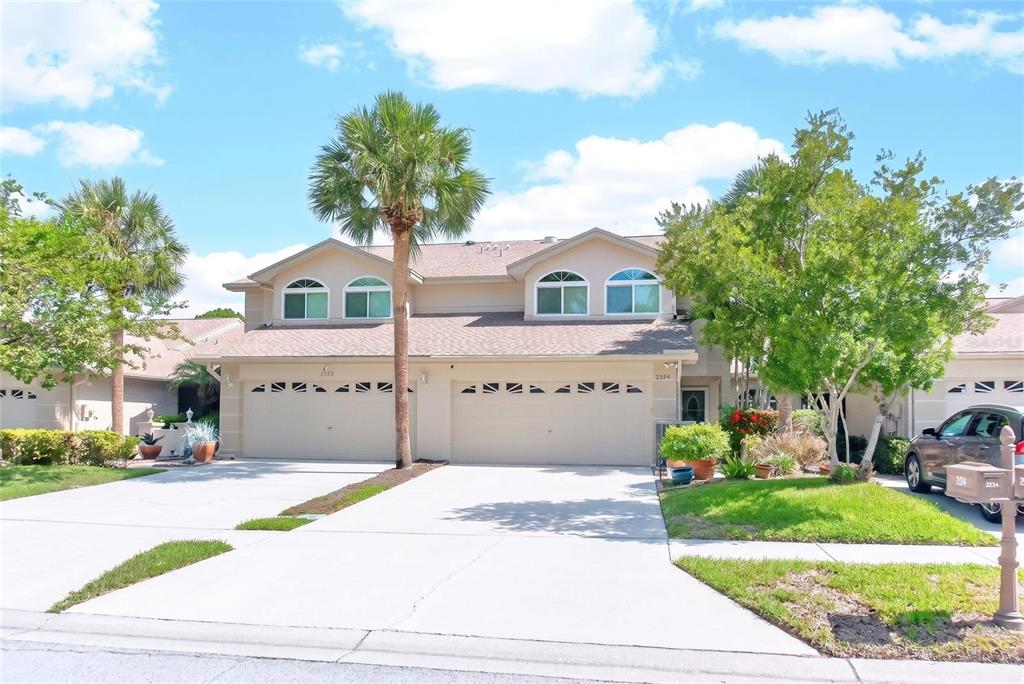 A two-story duplex with beige siding, two garage doors, and a palm tree in front — 2524 W BROOK LANE, CLEARWATER, FL