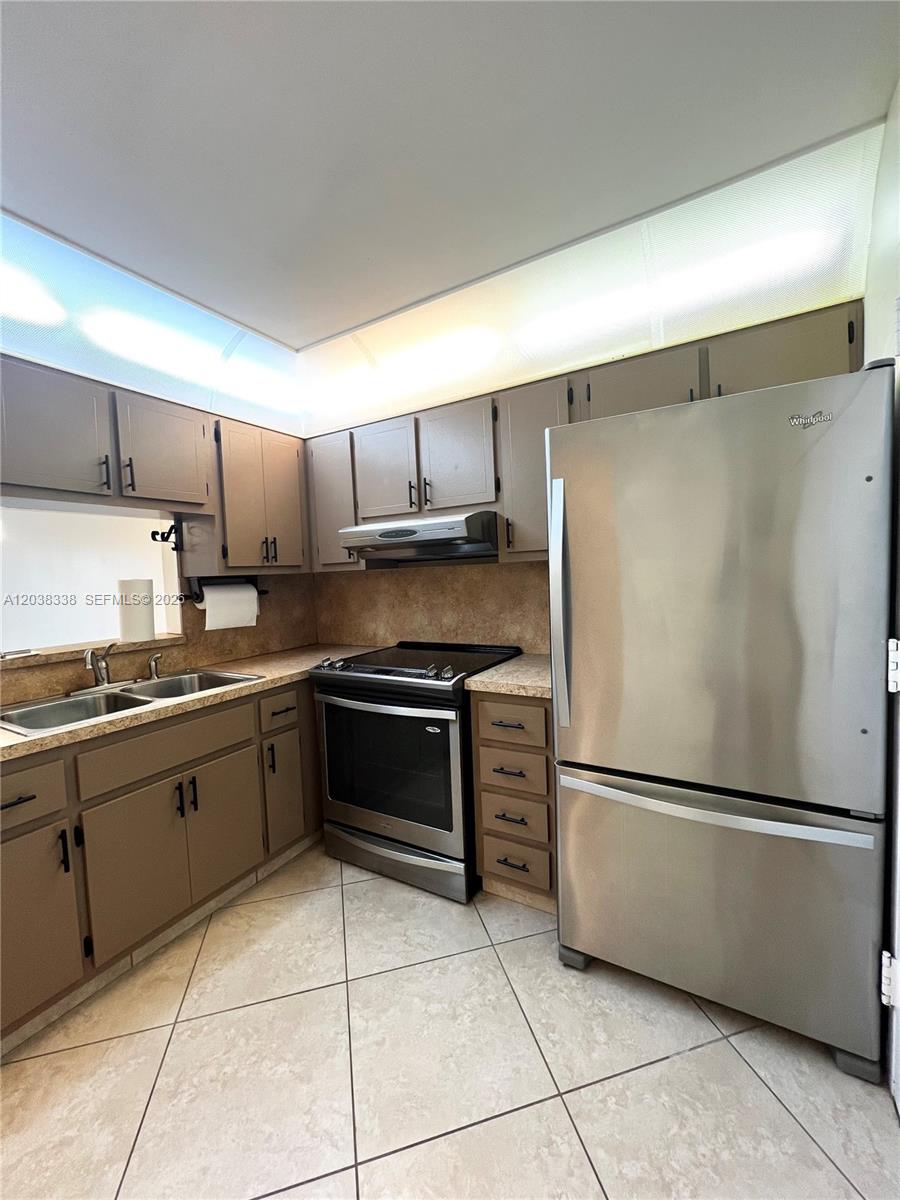 A kitchen features brown cabinets, stainless steel appliances, and light-colored tile flooring — 12035 NE 2nd Ave # A302, North Miami FL 33161, NORTH MIAMI, FL