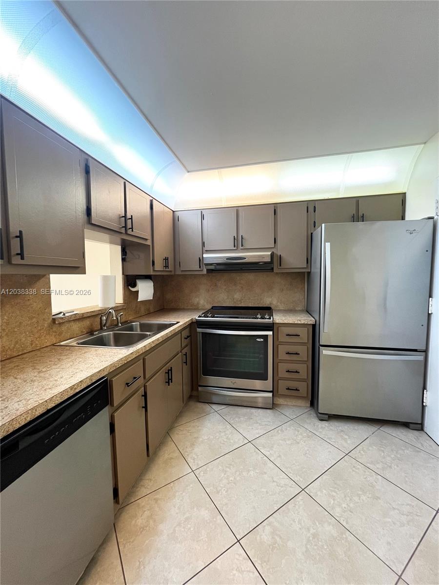 This kitchen features brown cabinets, stainless steel appliances, and beige countertops with tile flooring — 12035 NE 2nd Ave # A302, North Miami FL 33161, NORTH MIAMI, FL