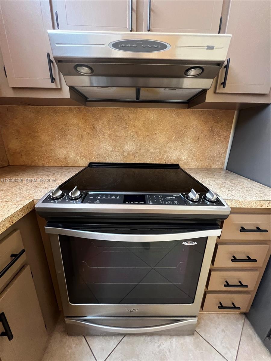 A stainless steel electric range and range hood are installed between tan cabinets and countertops — 12035 NE 2nd Ave # A302, North Miami FL 33161, NORTH MIAMI, FL