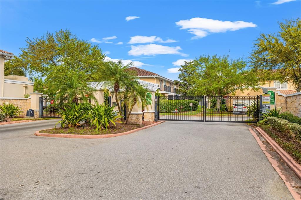 A gated entrance with a paved driveway, palm trees, and a white pergola structure — 184 VALENCIA CIRCLE, ST PETERSBURG, FL