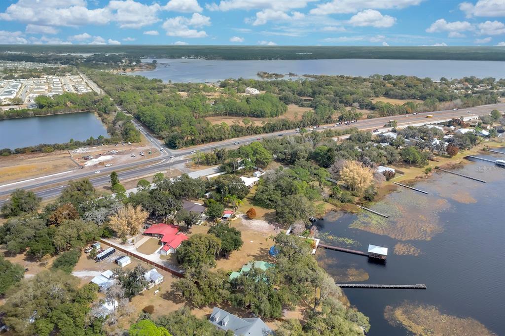 An aerial view shows a waterfront property with a red-roofed house near a highway — 5870 ALLIGATOR LAKE SHORE W, ST CLOUD, FL