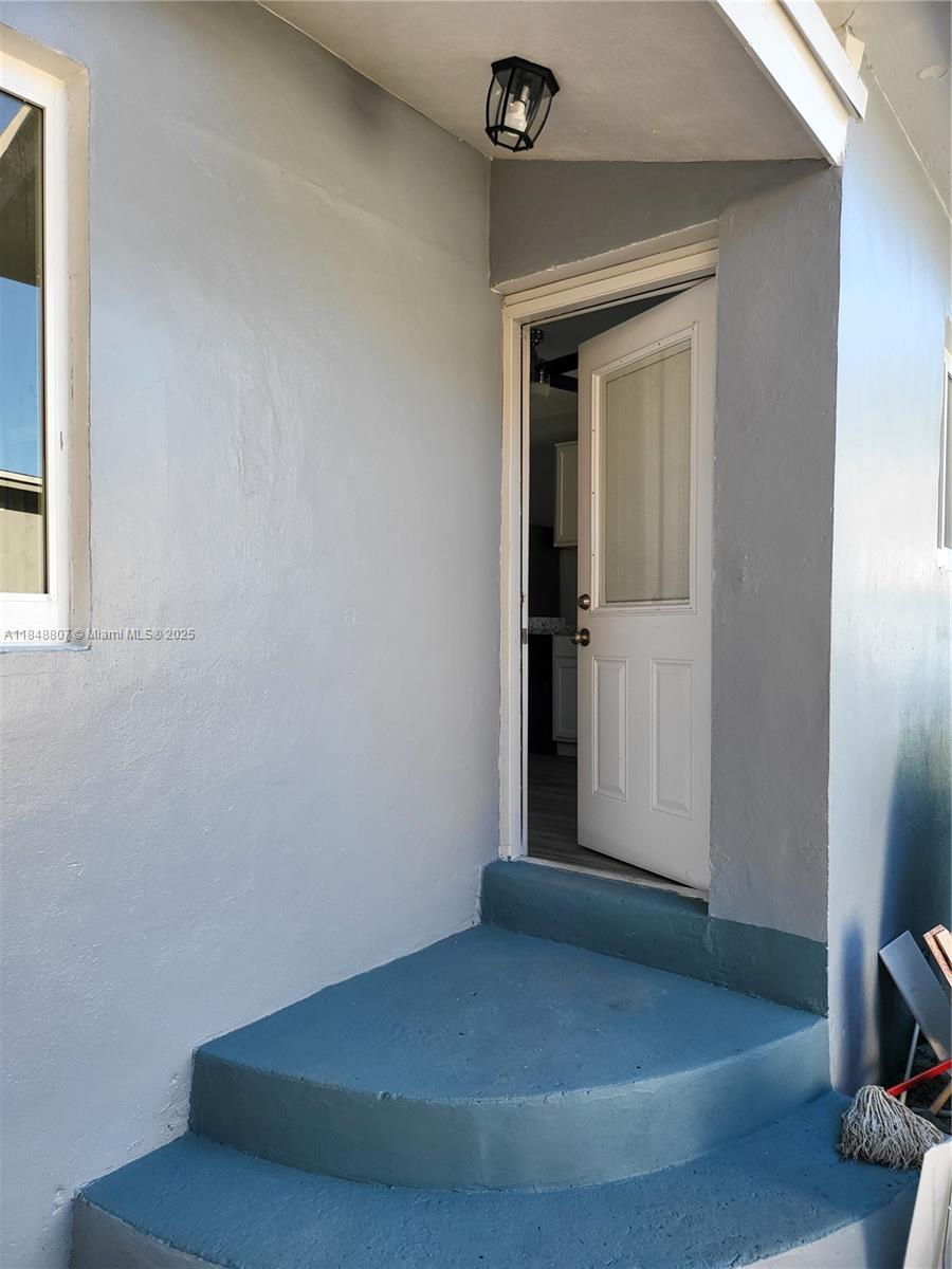 A gray exterior wall features a white door leading into a room with flooring — 123 NW 59th St # C, Miami FL 33127, MIAMI, FL