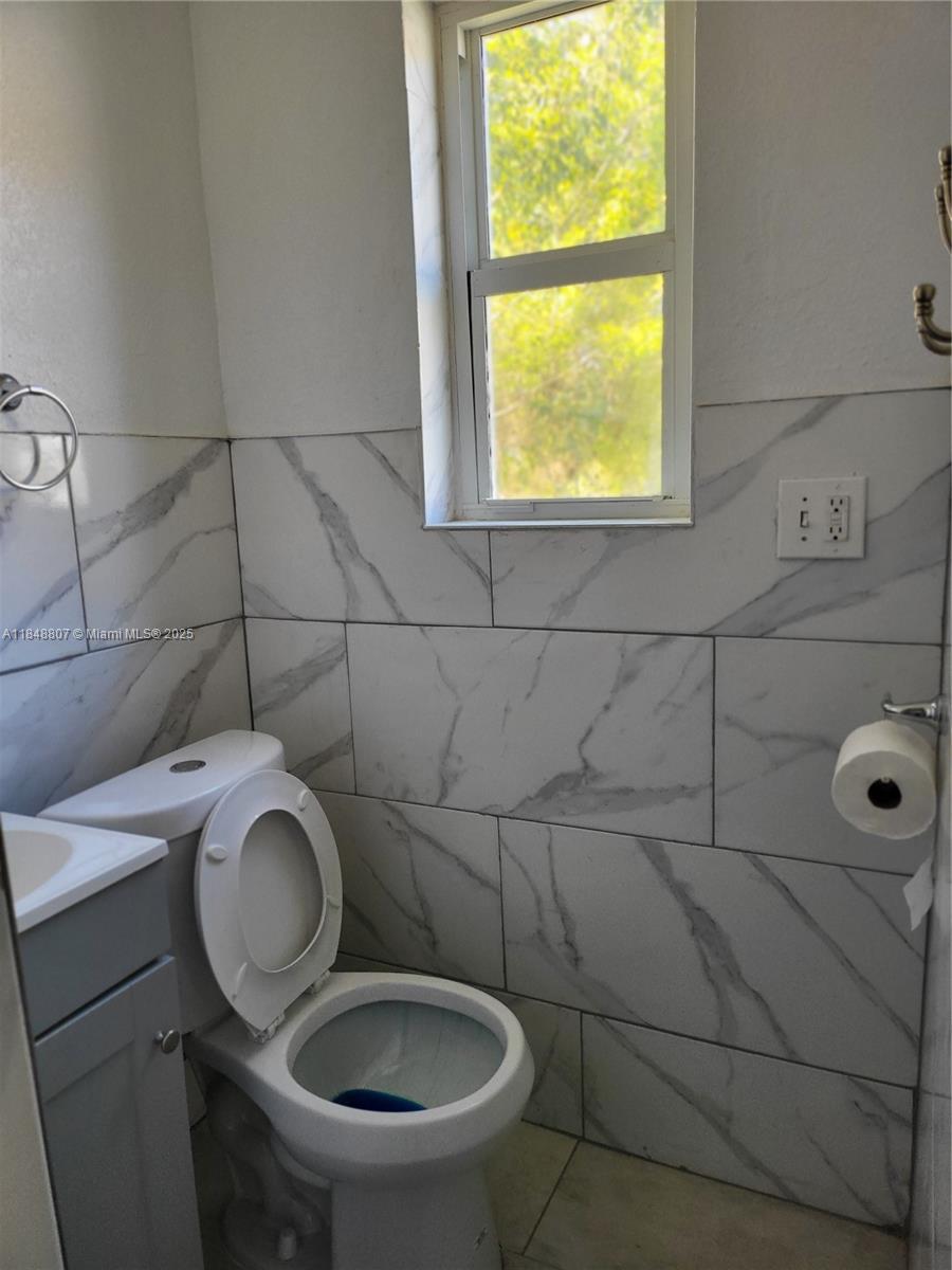 A bathroom features a white toilet, a grey vanity, and walls tiled with white marble — 123 NW 59th St # C, Miami FL 33127, MIAMI, FL